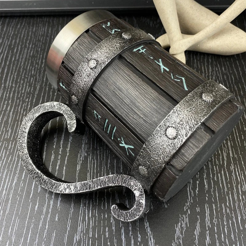 Aged metal mug with runes lying on a textured black surface.